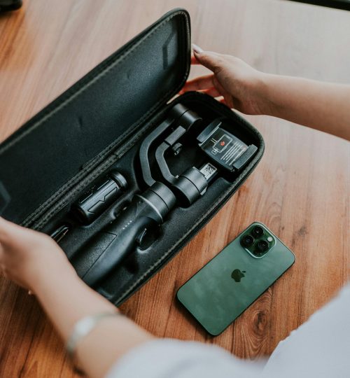 Hands open a case revealing camera equipment next to a smartphone on a wooden table.