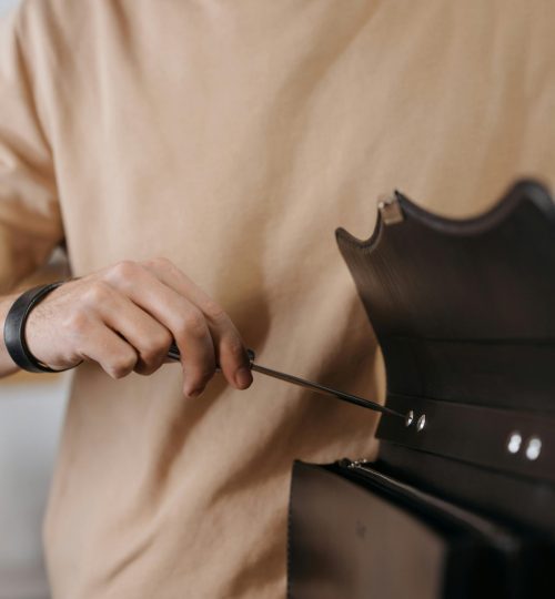 Close-up of a man using a screwdriver to repair a leather bag indoors.